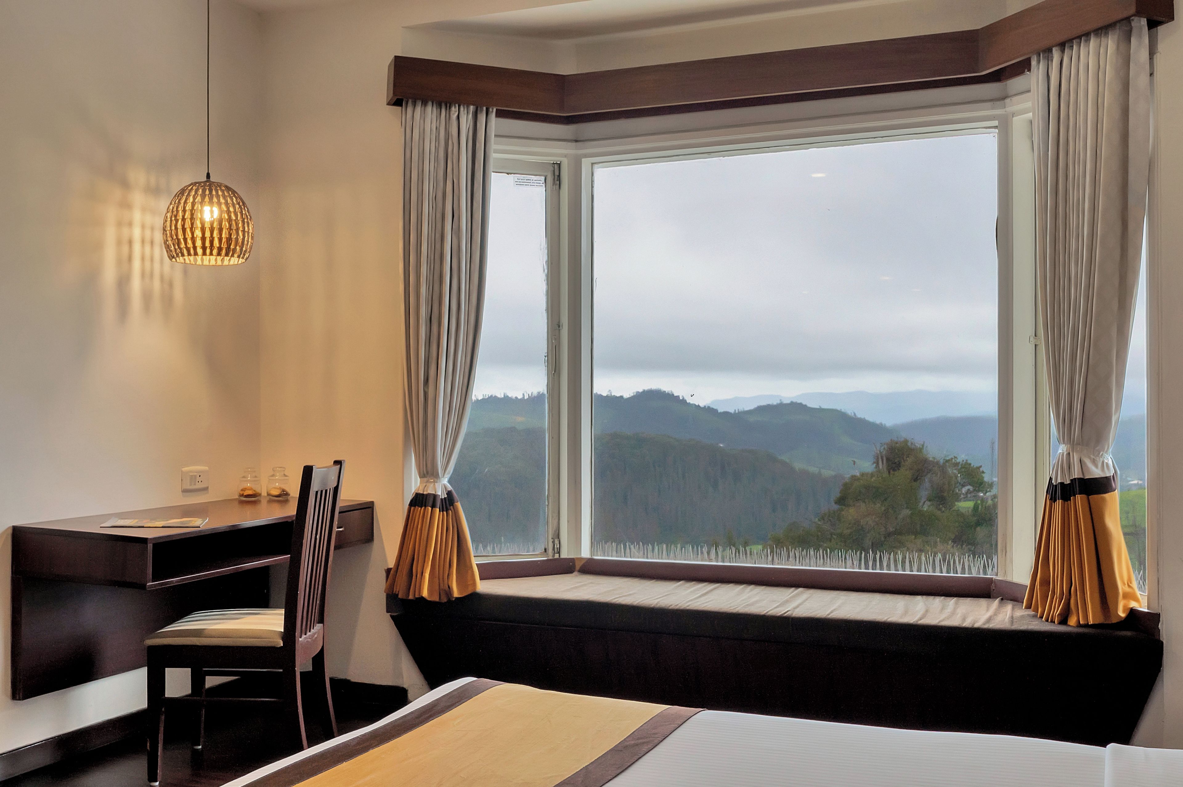 A hotel room with a large window, a desk, a chair, and a bed.