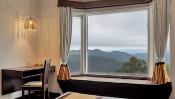 Une chambre d’hôtel avec une grande fenêtre, un bureau, une chaise et un lit.