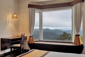 A hotel room with a large window, a desk, a chair, and a bed.