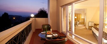 A balcony with a table set for dining, a chair, and a view of the city at dusk.