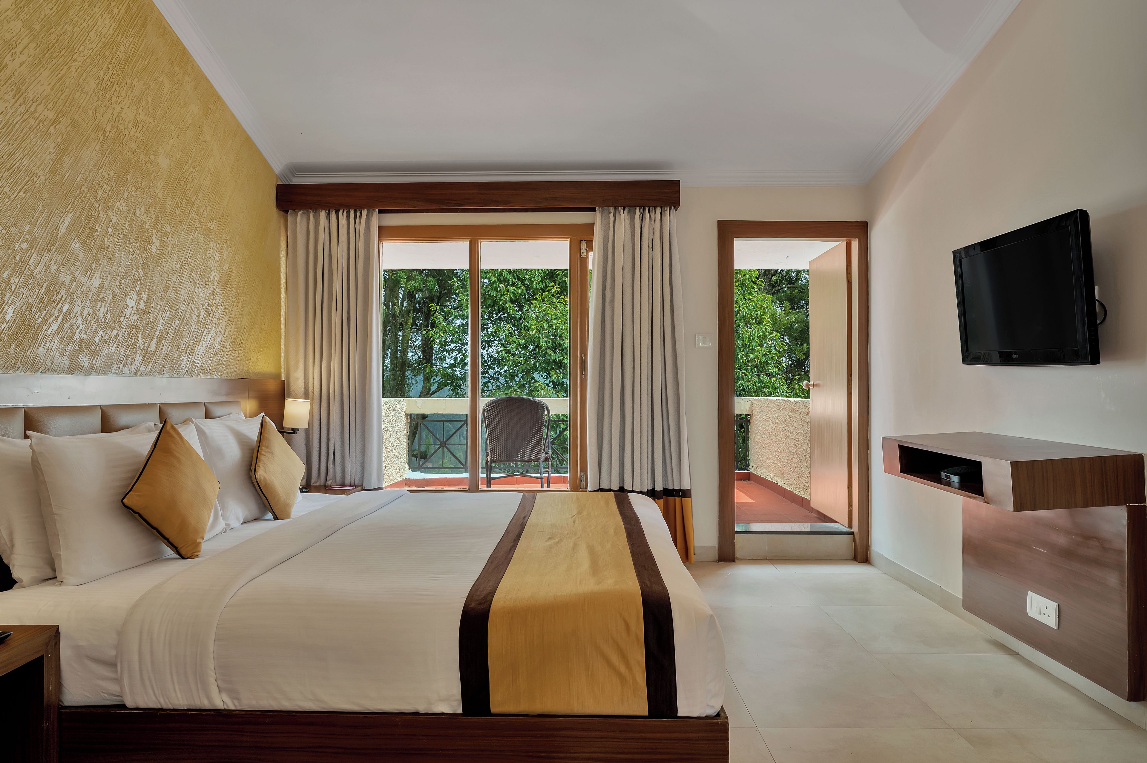 A hotel room with a bed, a TV mounted on the wall, and a balcony with a chair.