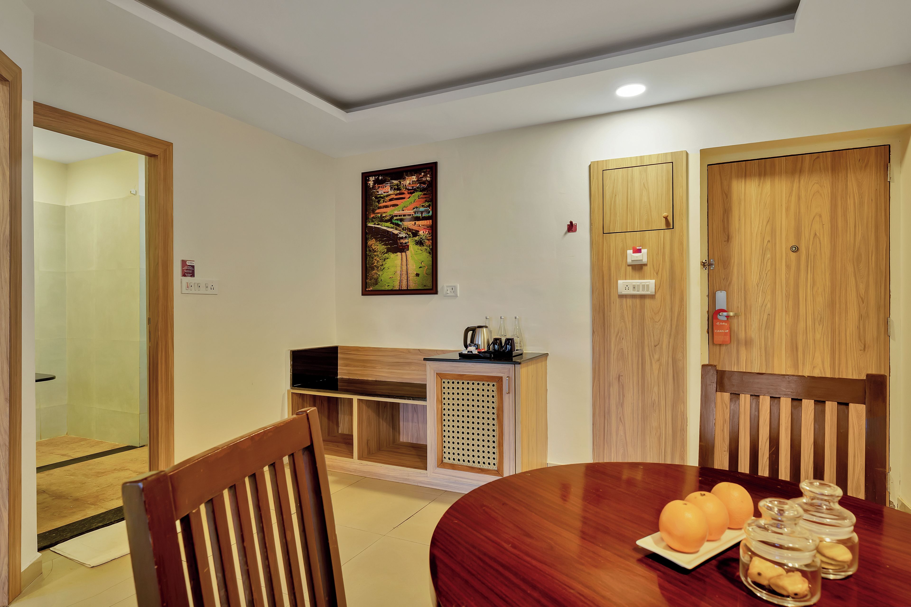 A compact dining area with a wooden table, chairs, a small kitchenette, and a painting on the wall.
