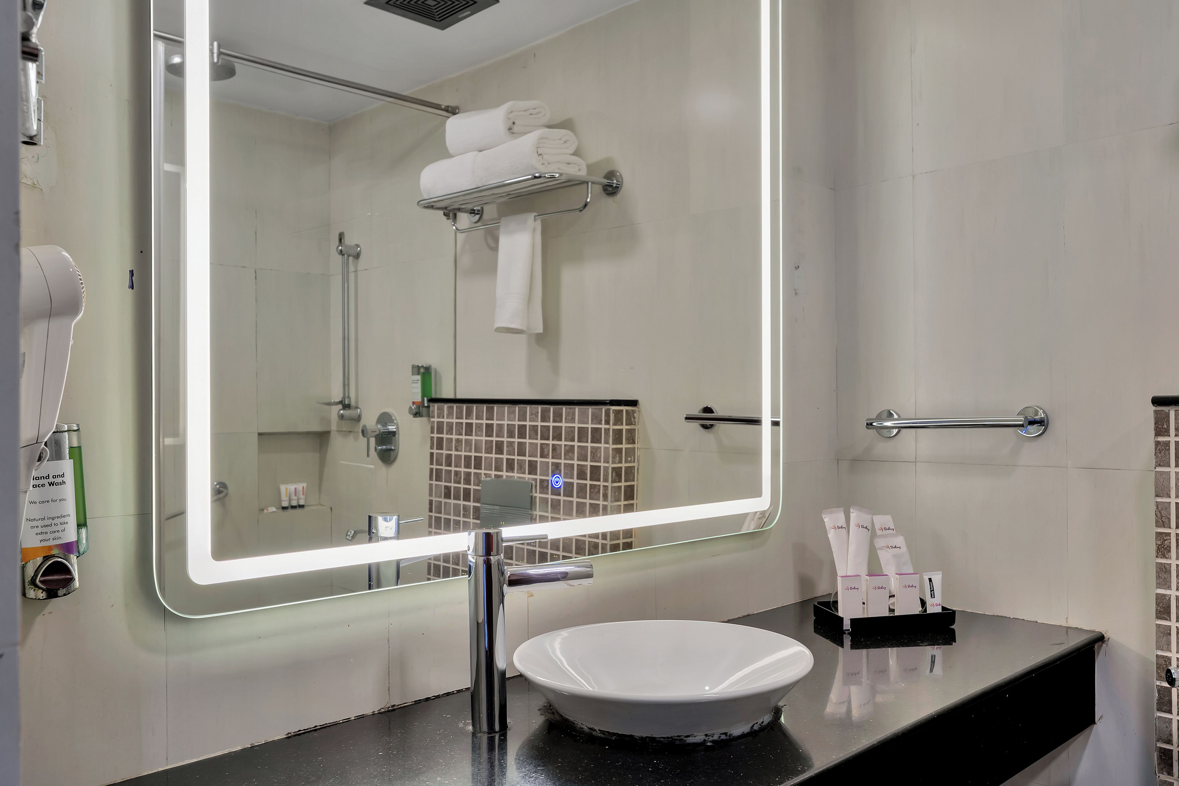 A bathroom with a large mirror, a sink, a towel rack, and toiletries.