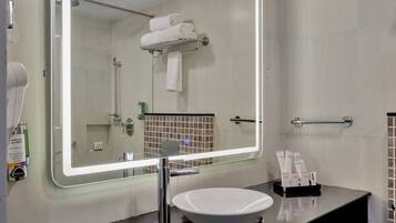 A bathroom with a large mirror, a sink, a towel rack, and toiletries.