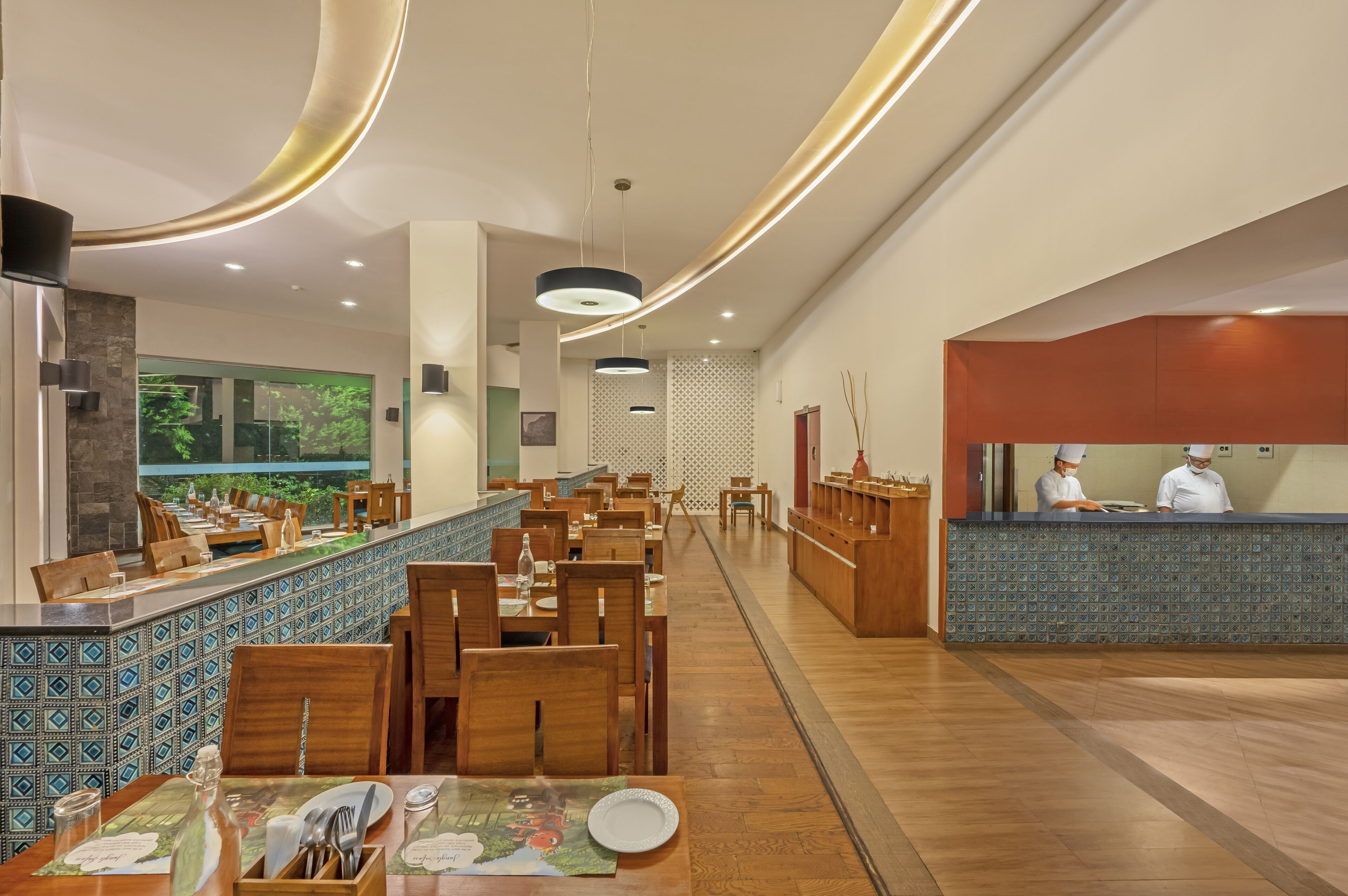 Un restaurante moderno con mesas y sillas de madera, un mostrador azulado y una zona de cocina con chefs.
