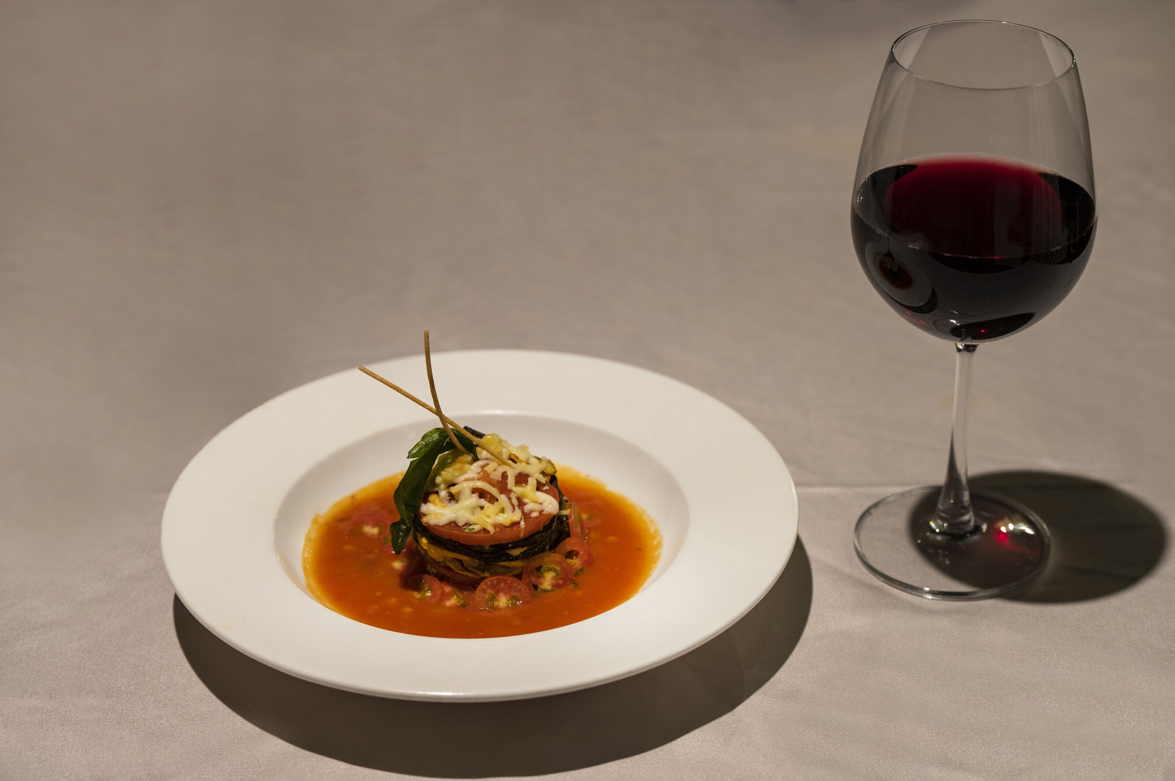 A white plate with a dish and a glass of red wine on a table.