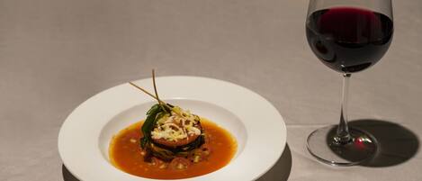 A white plate with a dish and a glass of red wine on a table.