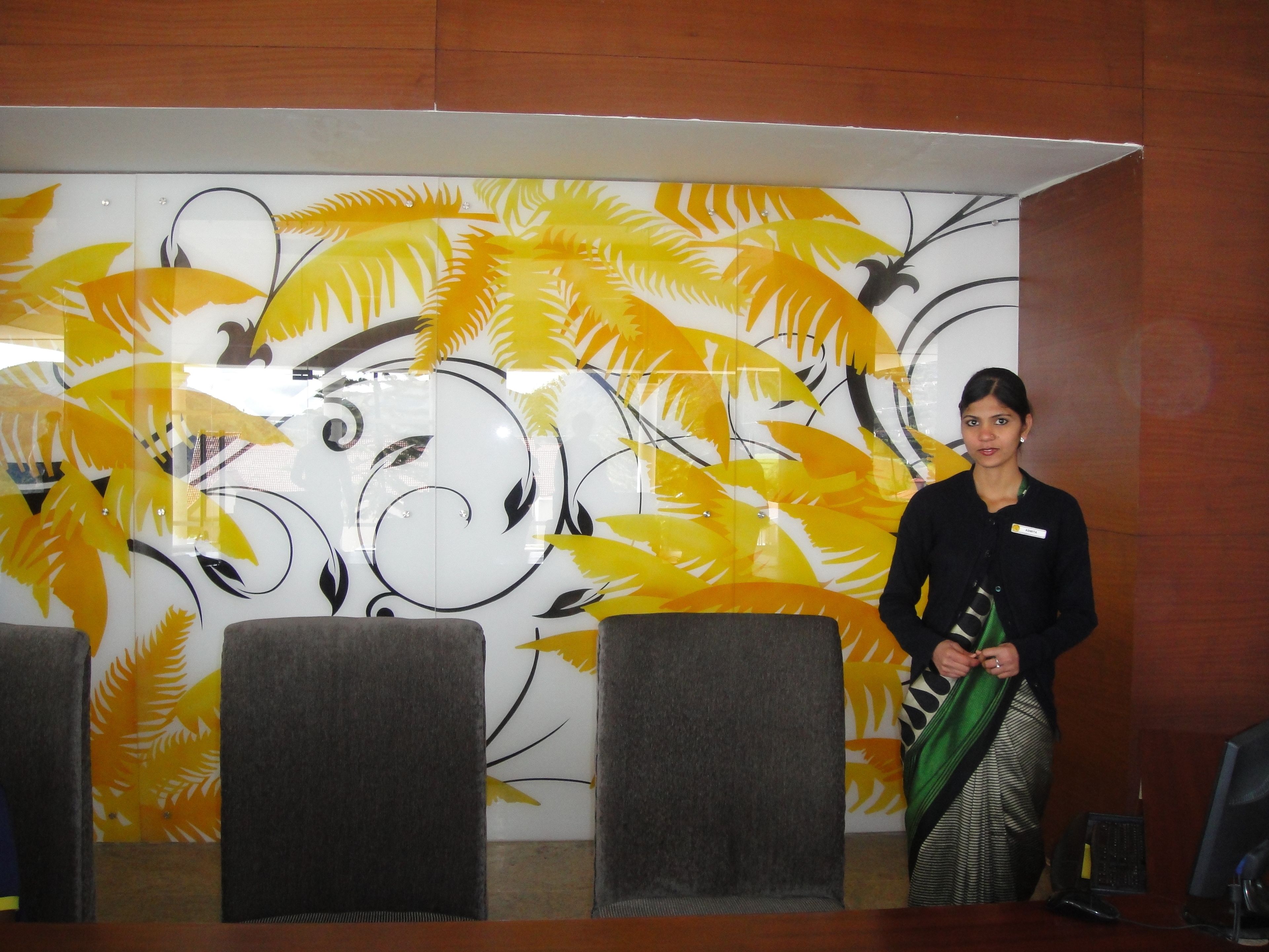 A reception area with a wall decorated with yellow and black leaf patterns, a seating area with grey chairs, and a wooden reception desk.