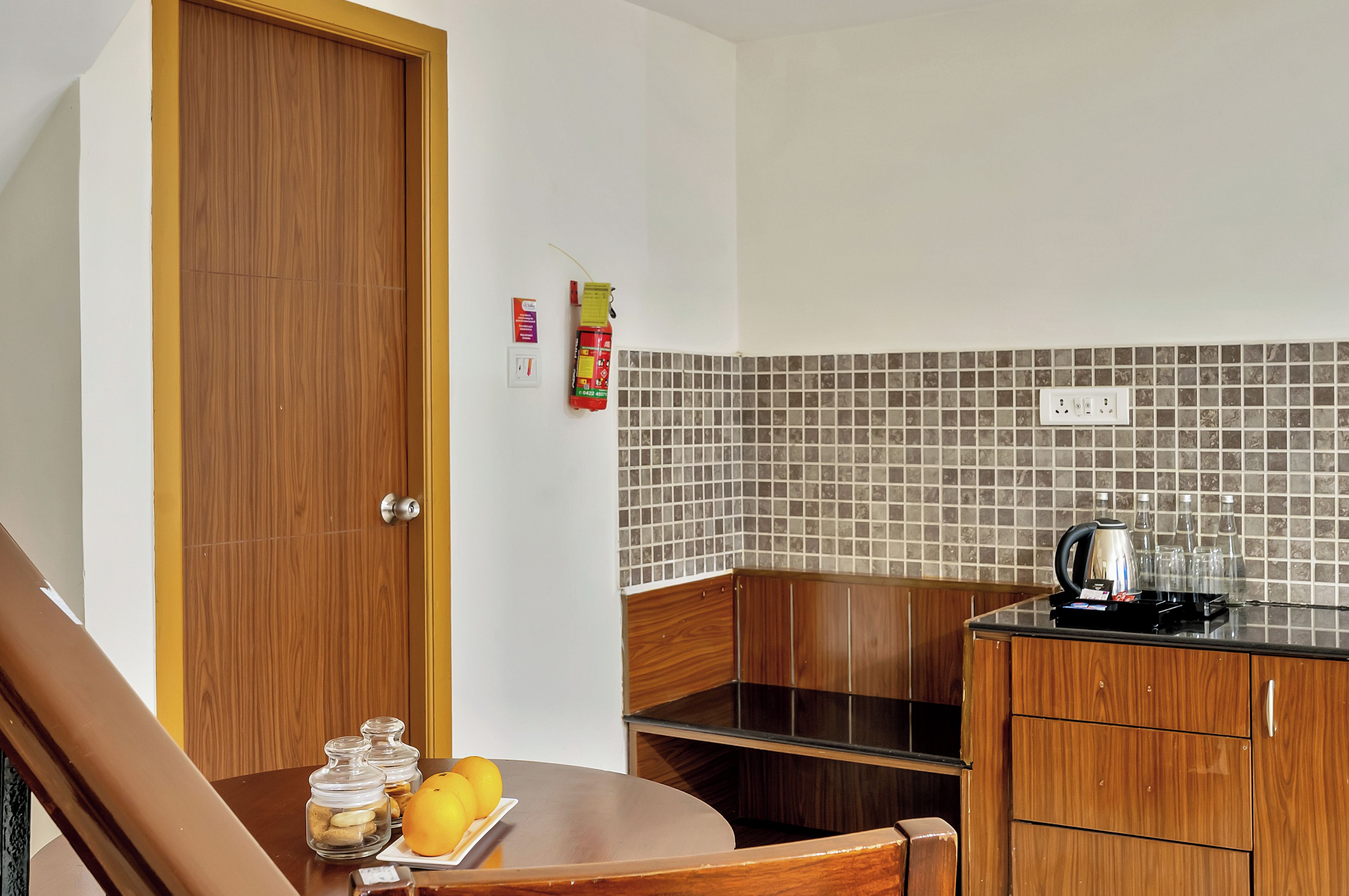 Una cocina compacta con puerta de madera, salpicadero de azulejos y encimera con hervidor y vasos.