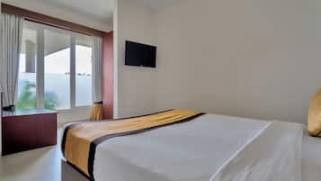 A hotel room with a bed, a television on the wall, and a window with curtains.