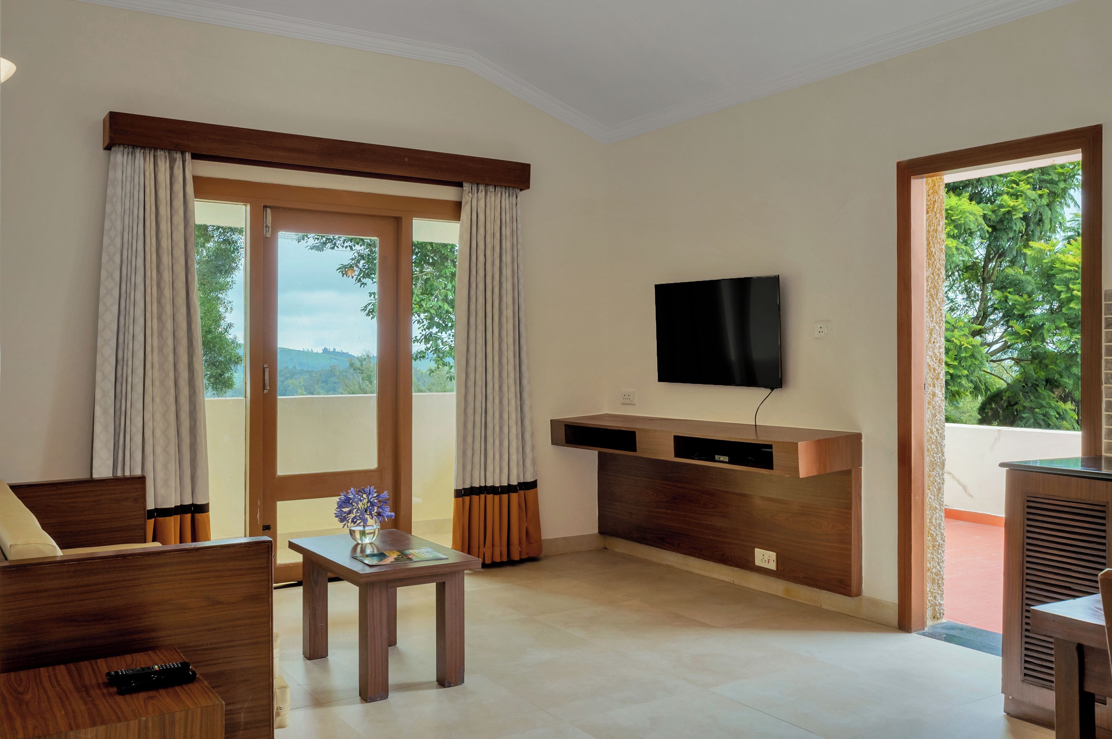 Una sala moderna con una televisión de pantalla plana montada en la pared, un mueble de madera para entretenimiento, un sofá, una mesa de centro con un florero y un ventanal con cortinas.