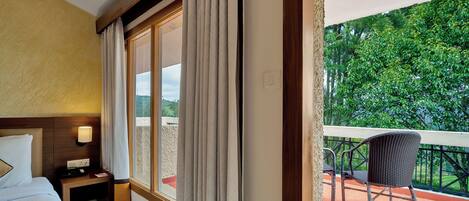 Una habitación de hotel con cama, mesita de noche, lámpara y vistas a un balcón con una silla.