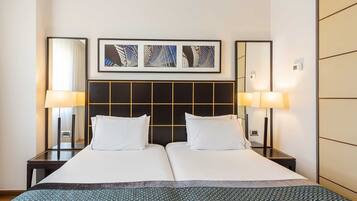 Una habitación de hotel con una cama grande, dos mesitas de noche y un cabecero con diseño geométrico.