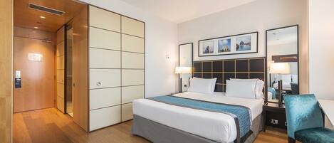 Una habitación de hotel con una cama grande, un escritorio, una silla y un armario.