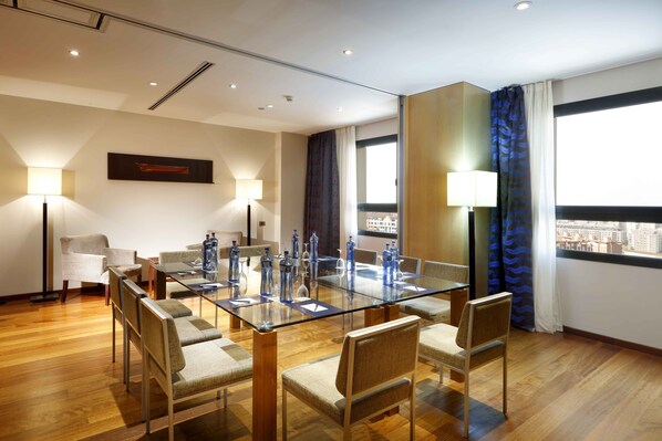 A modern hotel room with a glass dining table, comfortable seating, and large windows offering a city view. - Eurostars Gran Valencia Hotel (Valencia)
