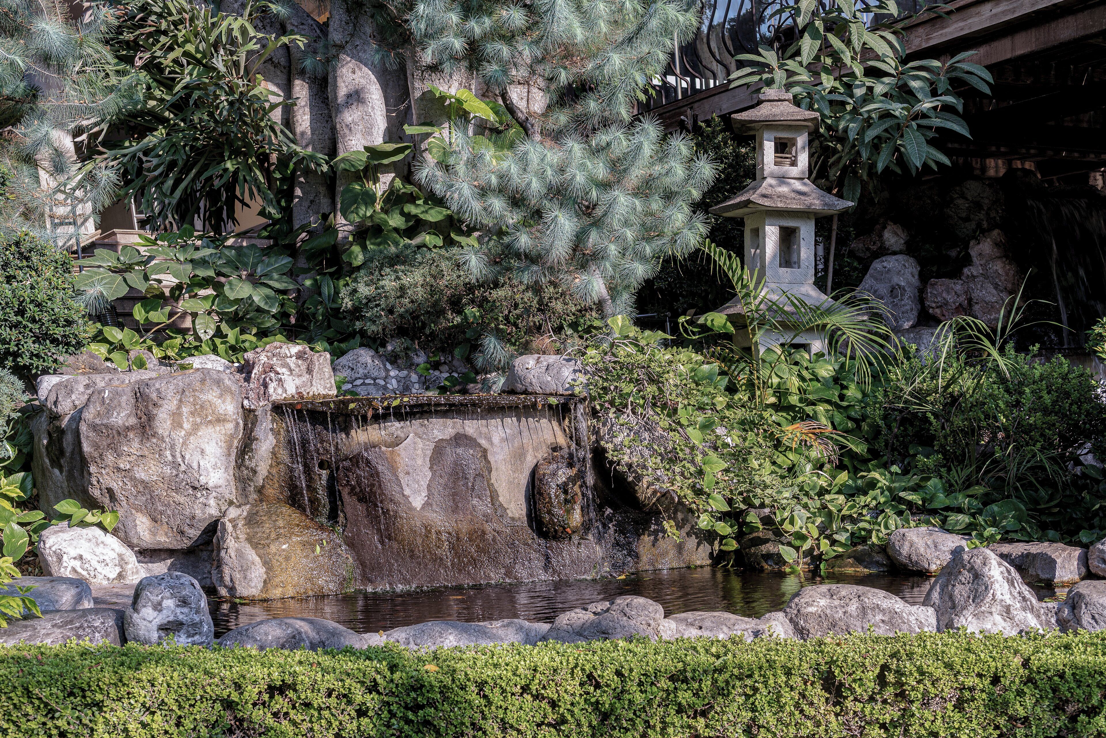 A tranquil garden with a small waterfall, large rocks, and a traditional pagoda.