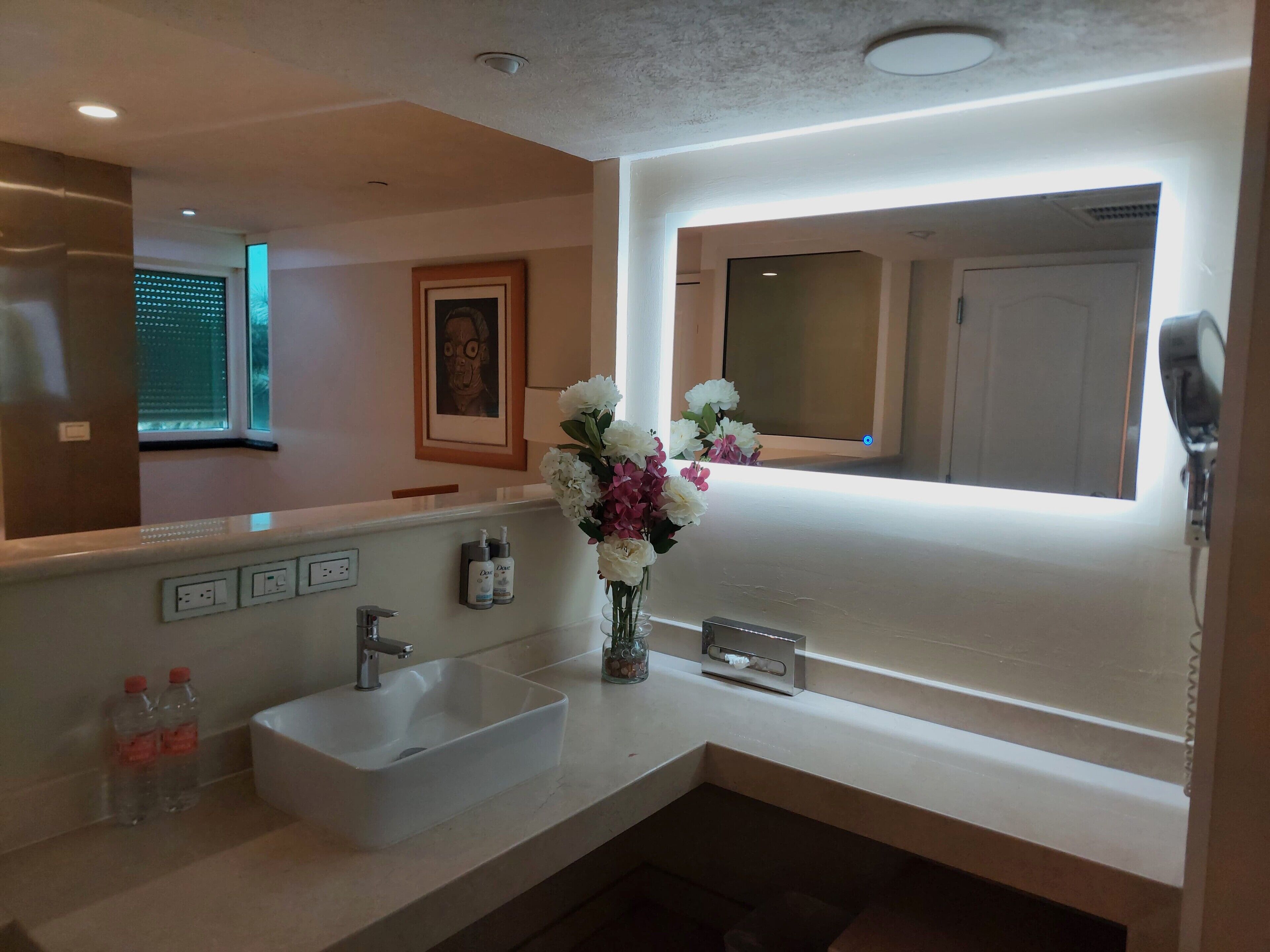 A modern bathroom with a white sink, a mirror, and a vase of flowers.