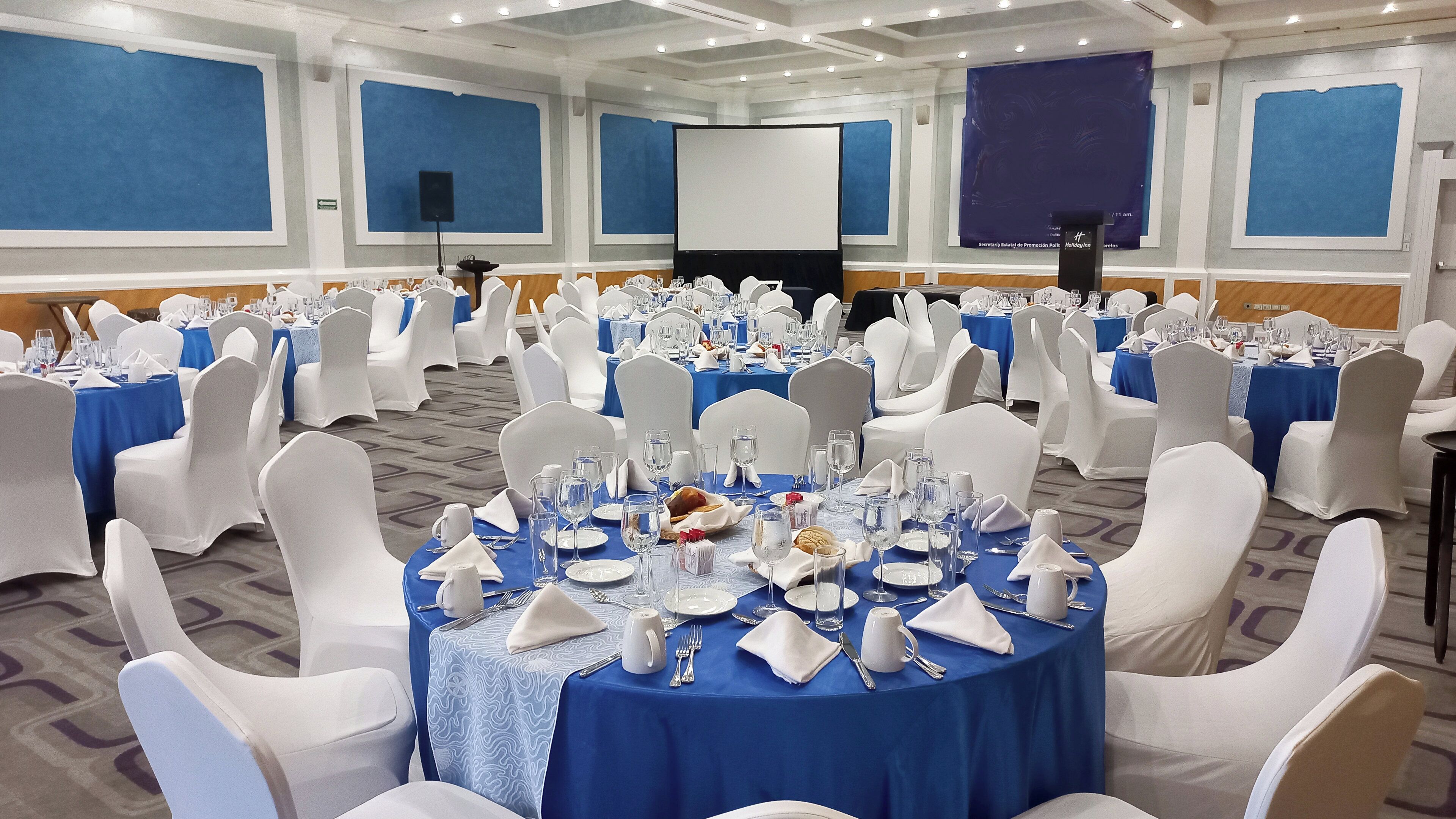Une salle de banquet avec des tables rondes, des chaises blanches et des nappes bleues.