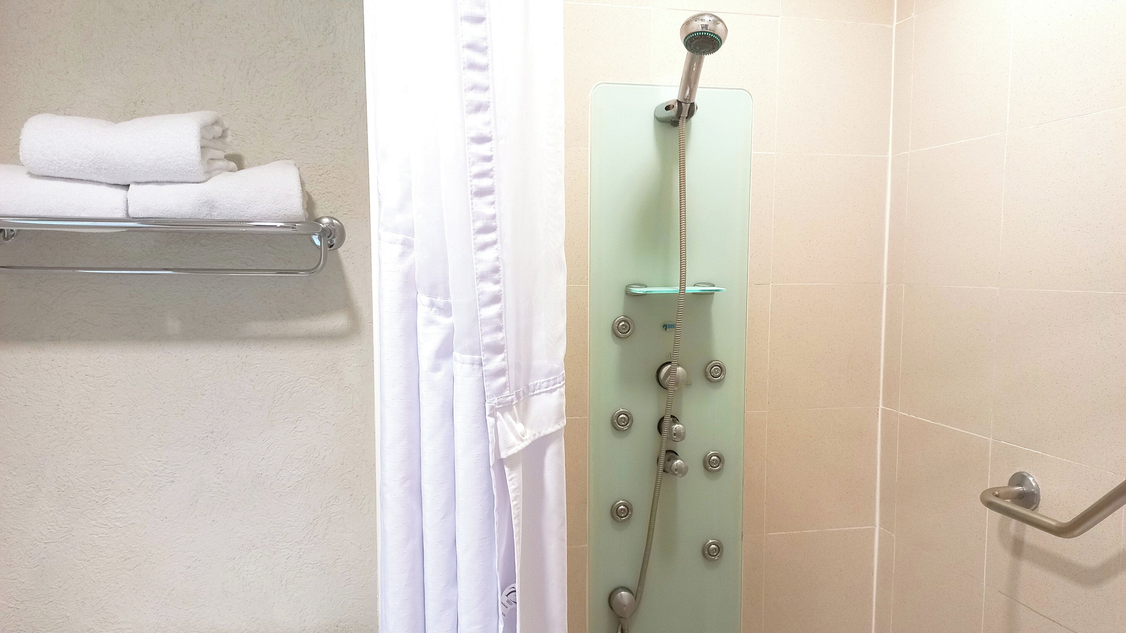 Ducha con cabezal de ducha de mano, cerramiento de vidrio y barra de apoyo en el lado derecho.