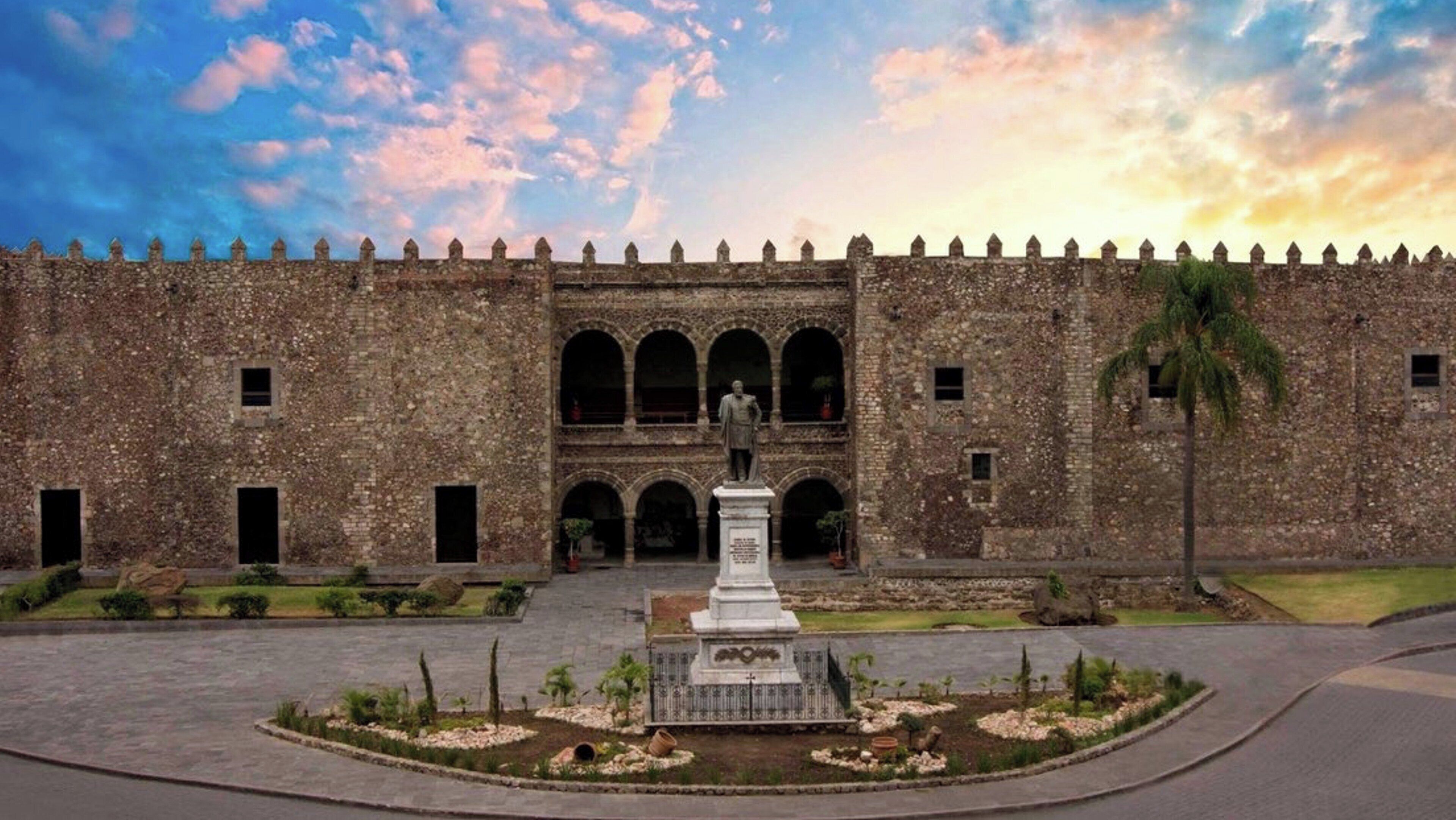A historic building with a central statue, arched windows, and a courtyard with plants.