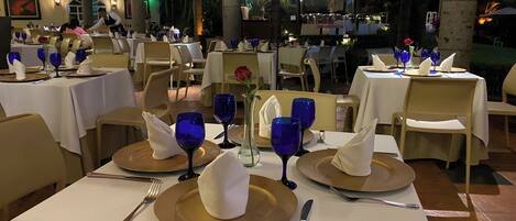 Restaurante con mesas dispuestas para comer, destacando copas azules y platos dorados.