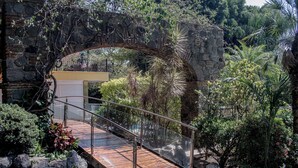 A stone arch bridge over a wooden pathway in a landscaped garden with various plants and a building in the background. - Holiday Inn Cuernavaca by IHG (Cuernavaca)