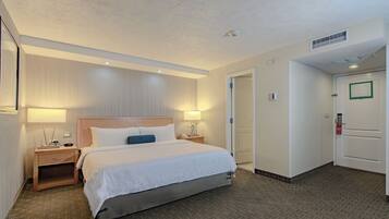 Habitación de hotel con una cama grande, mesitas de noche, una lámpara de pared y una puerta con un cartel verde.