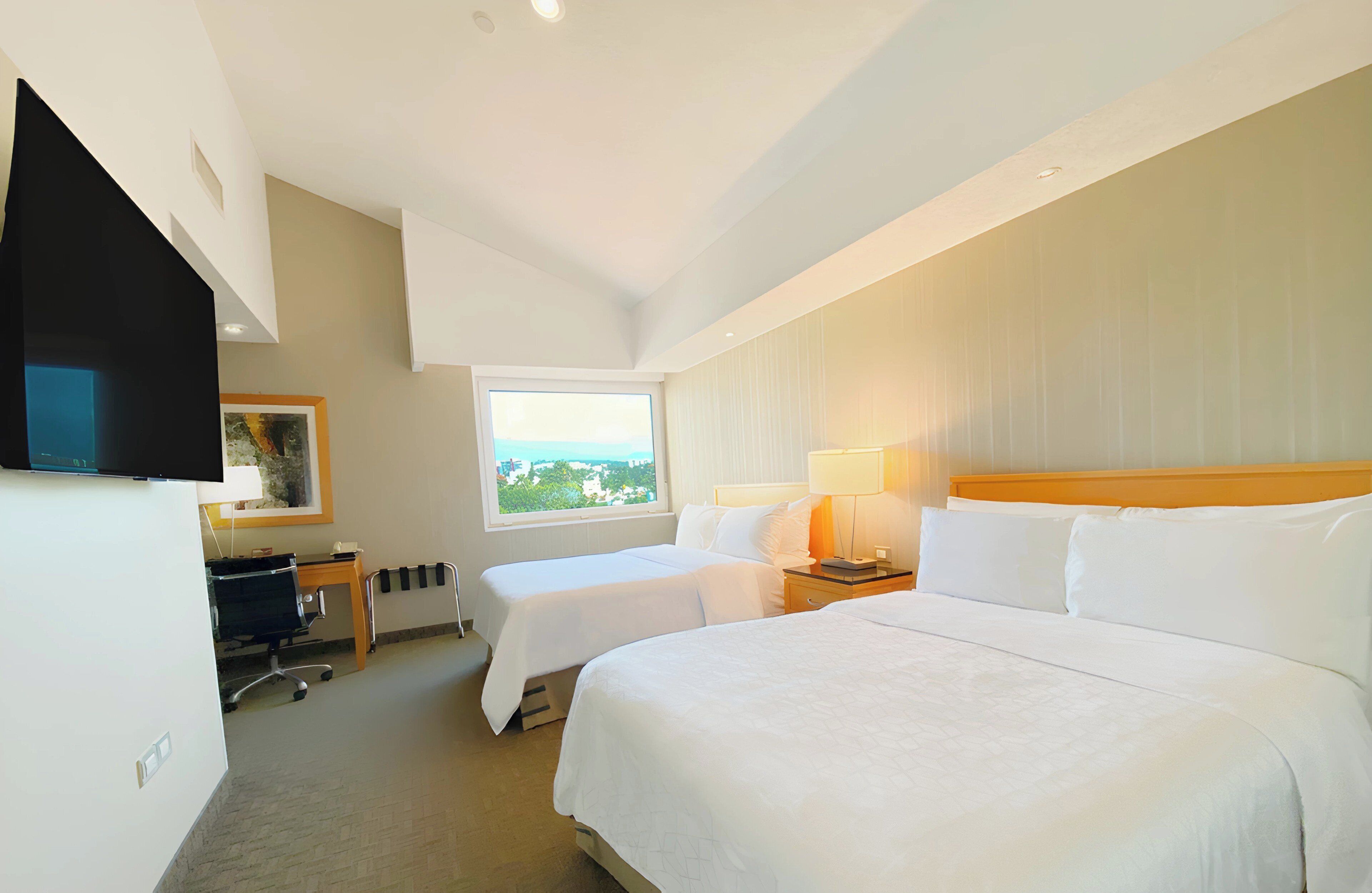 Habitación de hotel con dos camas, un escritorio con silla, televisión, ventana con vistas y una lámpara.