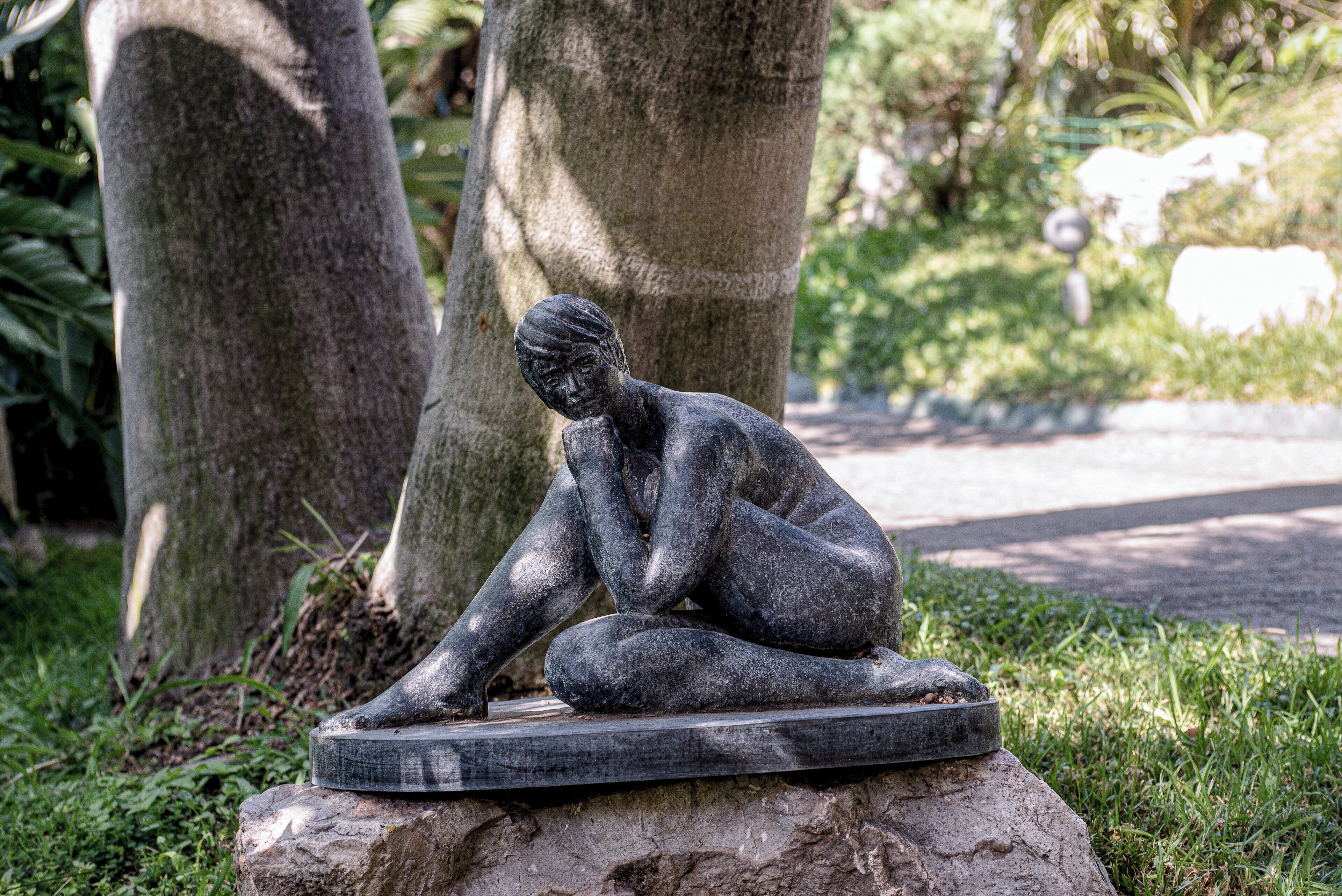 A sculpture of a seated figure on a stone base in a park setting.