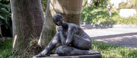 Una escultura de una figura sentada sobre un pedestal de piedra en un parque.