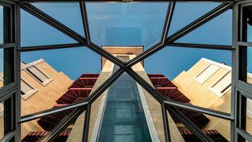 Vista a través de una estructura de ventana geométrica, reflejando edificios con estilos arquitectónicos diversos y un cielo azul claro.