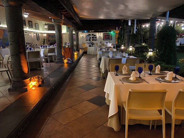 An outdoor dining area with tables set for service, featuring a tiled floor and columns. - Holiday Inn Cuernavaca by IHG (Cuernavaca)