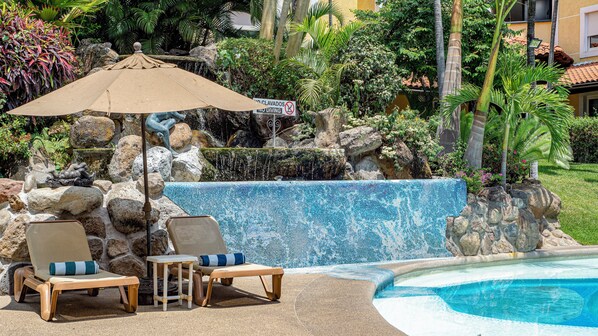 A pool area with lounge chairs, a decorative rock wall, and a waterfall feature.