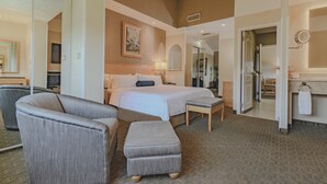 A hotel room with a bed, a sitting area with a chair and ottoman, a bathroom with a sink and mirror, and a hallway leading to other rooms. - Holiday Inn Cuernavaca by IHG (Cuernavaca)