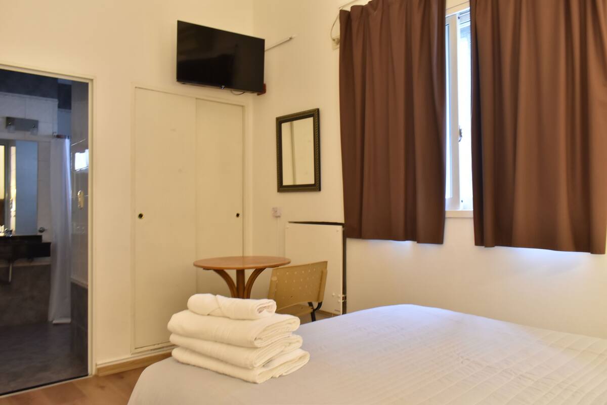 A hotel room with a bed, a TV mounted on the wall, a small table, and a chair.