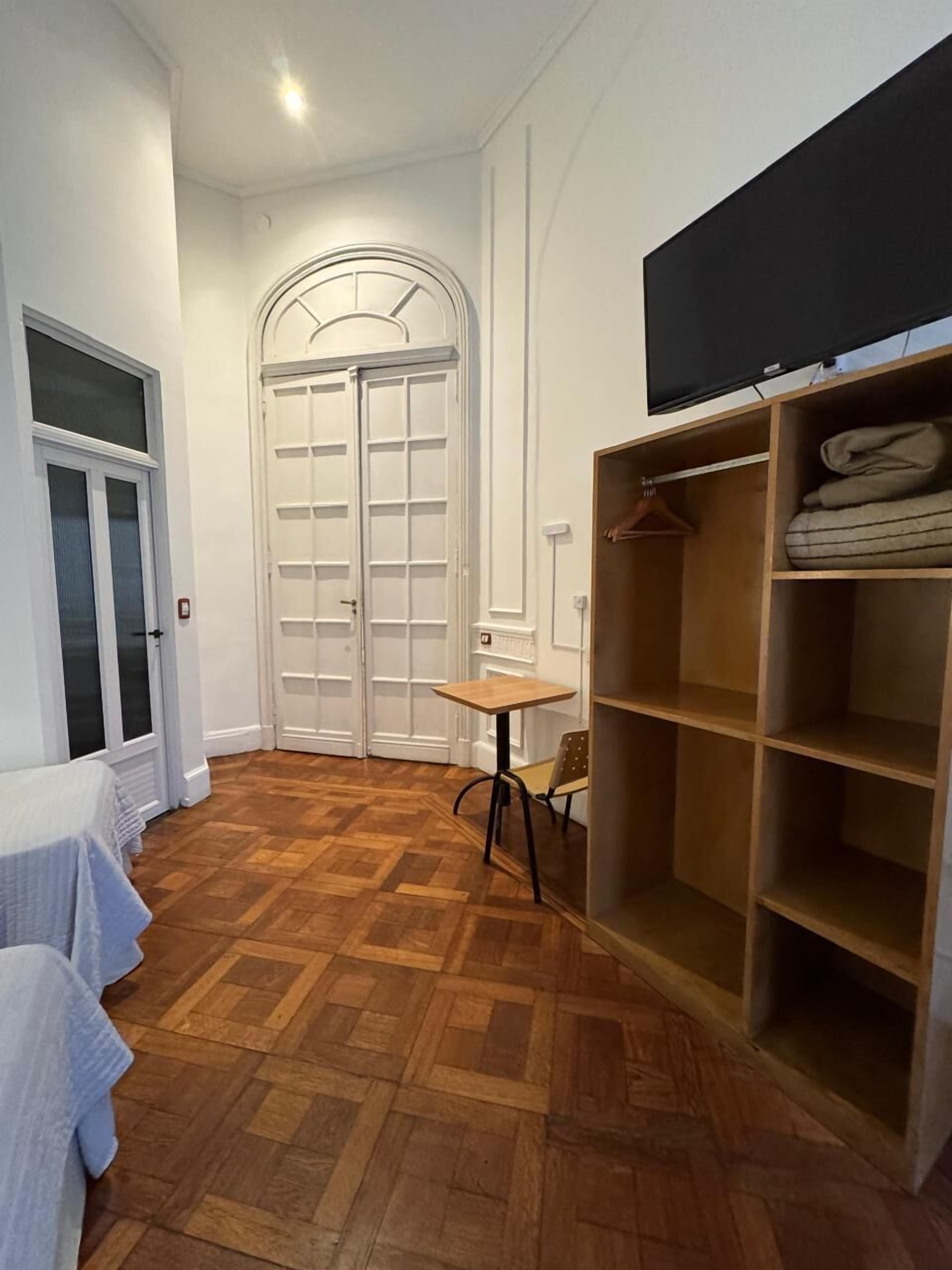A room with a wooden parquet floor, a white door with glass panels, a small table, and a shelving unit with folded clothes.