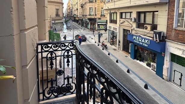 A balcony with a metal railing overlooking a street with buildings, a restaurant, and a clear sky. - Hotel Frossard (Buenos Aires)
