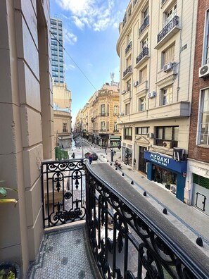 A balcony with a metal railing overlooking a street with buildings, a restaurant, and a clear sky. - Hotel Frossard (Buenos Aires)