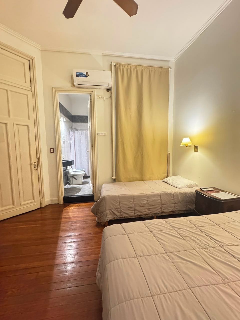 A hotel room with a bed, a nightstand, a lamp, a ceiling fan, and an air conditioning unit.