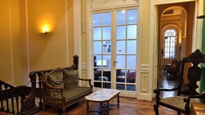 A room with a wooden floor, a sofa, a table, and a chair. There is a door with glass panels and a view of another room. - Hotel Frossard (Buenos Aires)