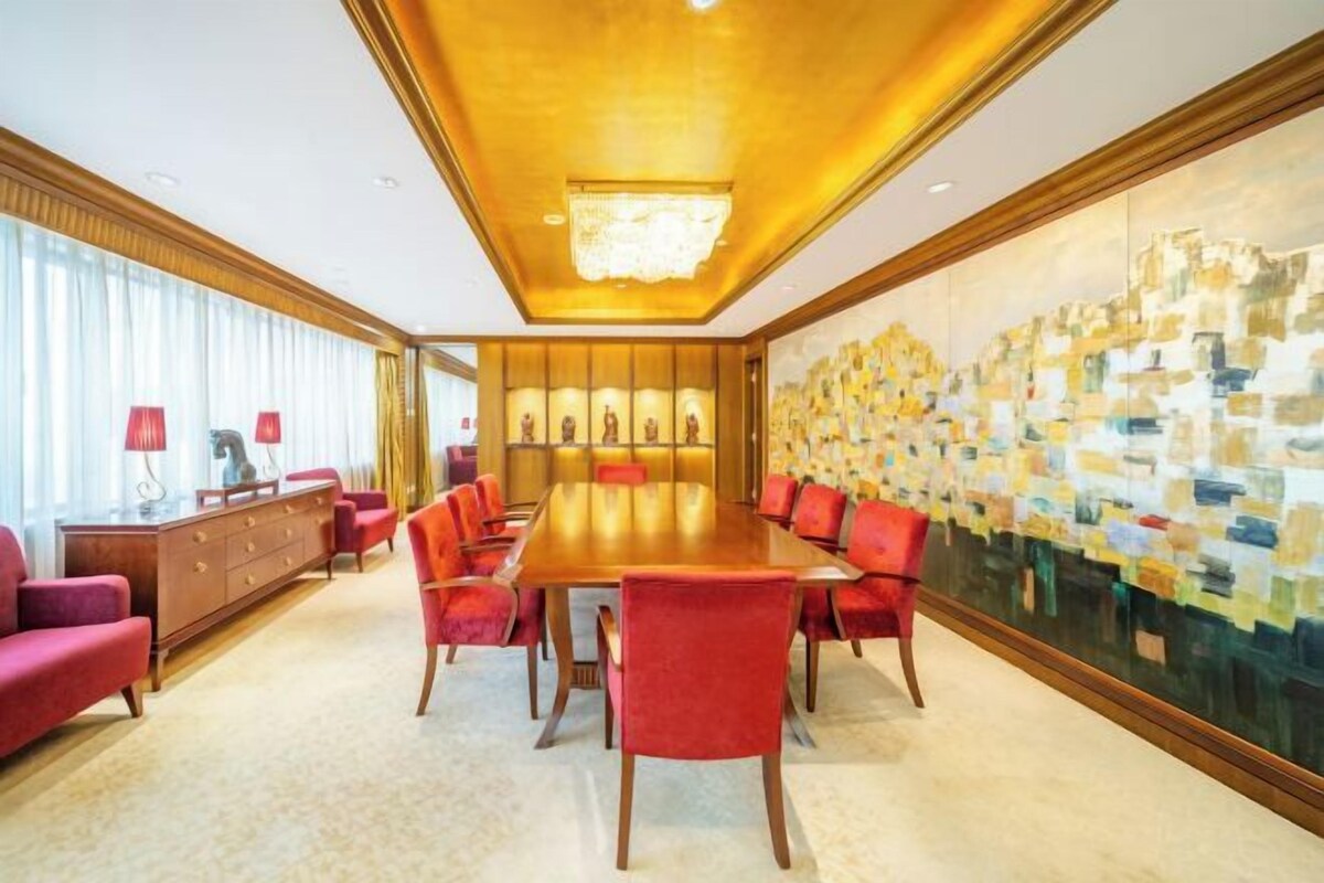 Un salón de conferencias con una larga mesa y sillas rojas, un aparador de madera y un cuadro abstracto grande en la pared.