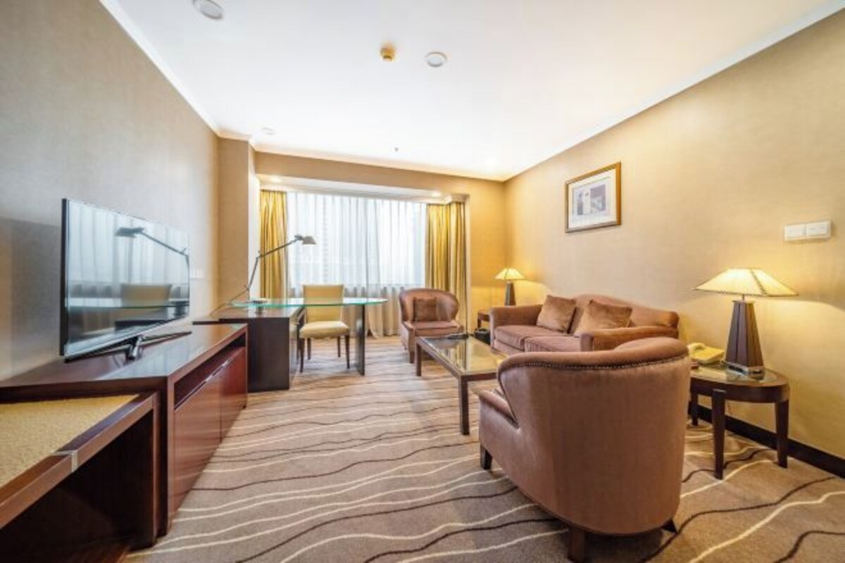 Habitación de hotel con televisión, sofá, sillón y zona de comedor con mesa y sillas.