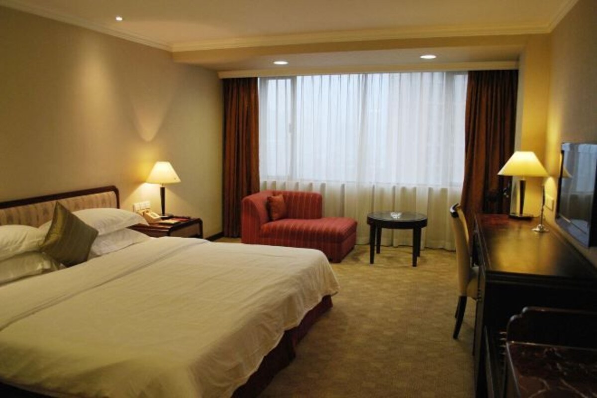 Una habitación de hotel con una cama grande, un escritorio con televisor, una silla y una mesita.