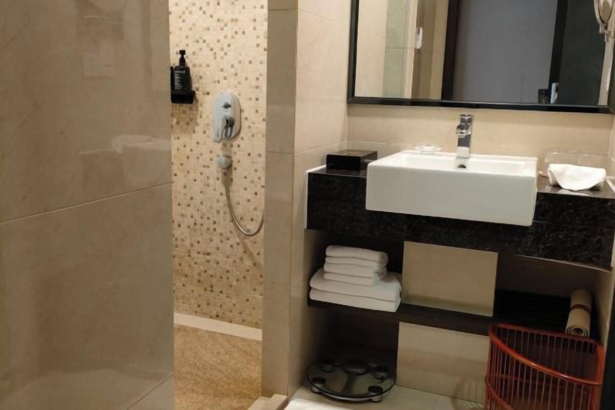 Un baño con lavamanos blanco, un espejo, toallero y zona de ducha.