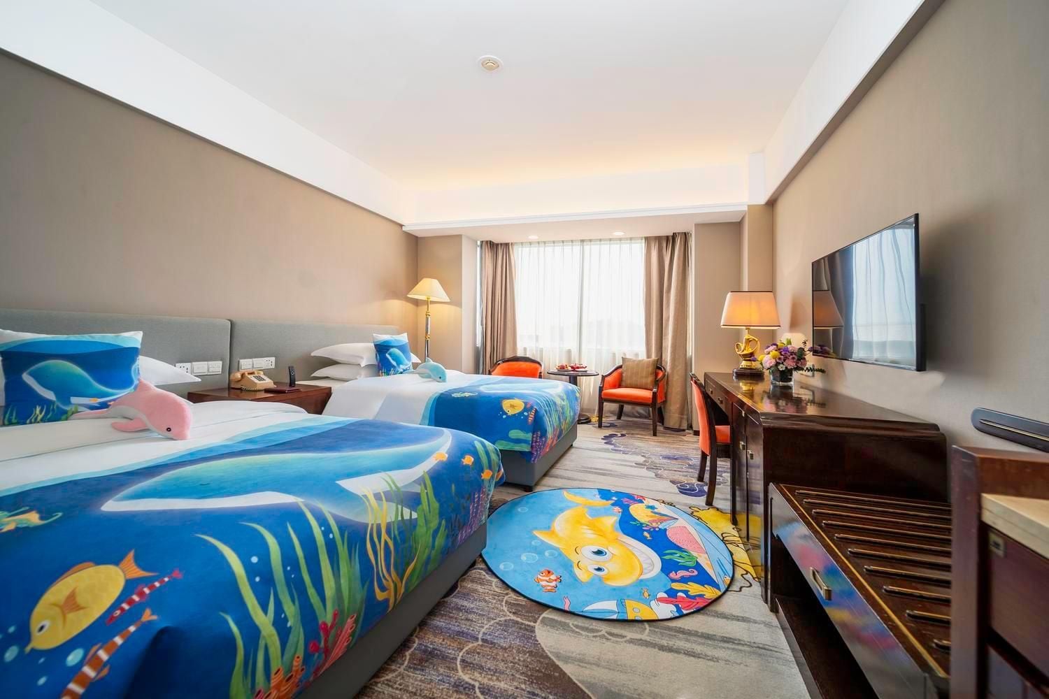 Habitación de hotel con dos camas, un escritorio, una silla, un televisor y una ventana con cortinas.
