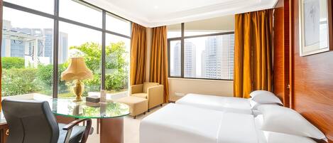 A hotel room with a bed, a desk with a chair, a lamp, and large windows with curtains.