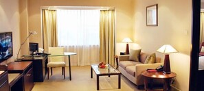 Ein Hotelzimmer mit Schreibtisch, Stuhl, Sofa, Couchtisch, Lampen und einem Fernseher.