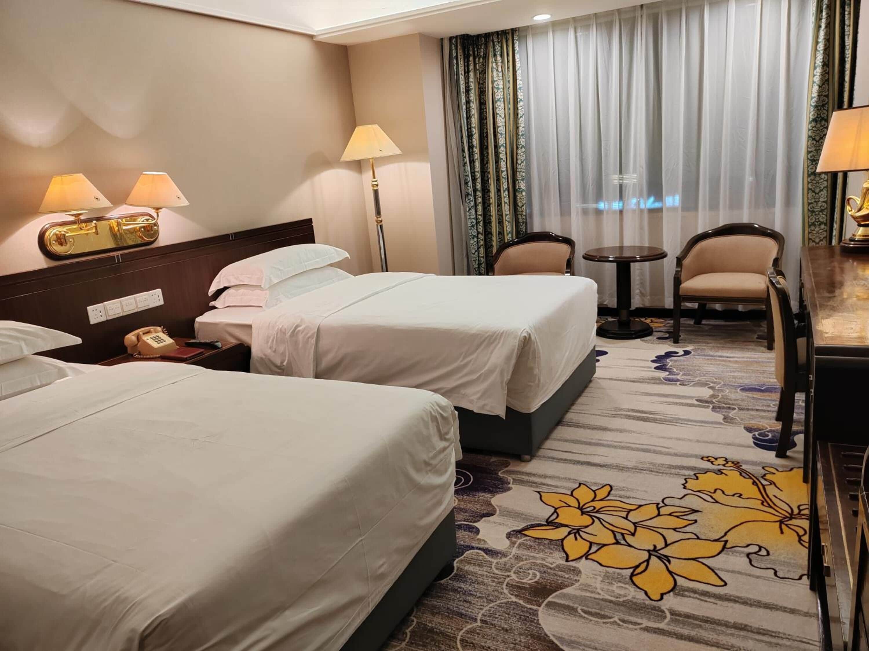 Une chambre d’hôtel avec deux lits, un bureau, une chaise, un téléphone et une lampe.