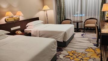Une chambre d’hôtel avec deux lits, un bureau, une chaise, un téléphone et une lampe.