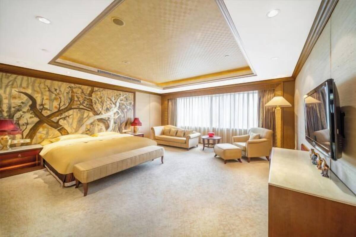 Habitación de hotel con una cama grande, un sofá, una mesita, un televisor y un cuadro en la pared.